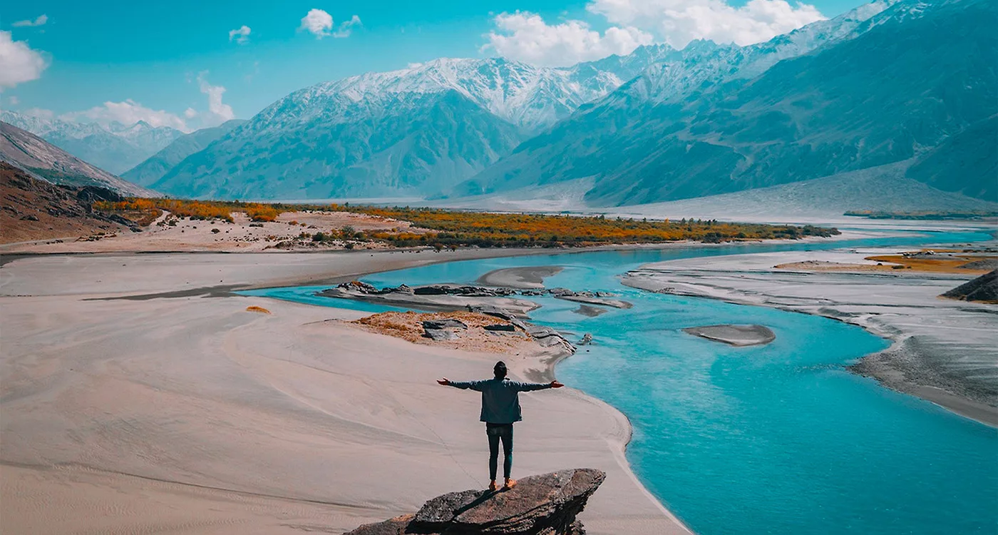 Homme bras écarté devant un paysage avec rivière et montagnes